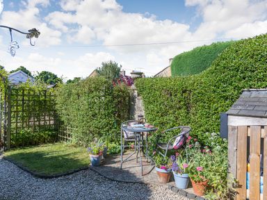 A small garden with a table and two chairs surrounded by potted plants and hedges at Puffitts Cottage in Bourton-on-the-Water
