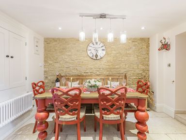 A dining room with a wooden table red chairs a stone wall and a clock at Puffitts Cottage in Bourton-on-the-Water