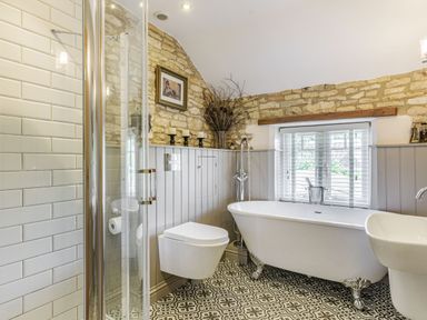 A bathroom with a freestanding bathtub a toilet a sink a shower with glass door and patterned floor tiles at Puffitts Cottage in Bourton-on-the-Water