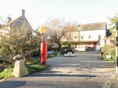 An outdoor scene with stone buildings a red vintage petrol pump and a car covered in greenery with a halt motoring museum sign at Puffitts Cottage in Bourton-on-the-Water