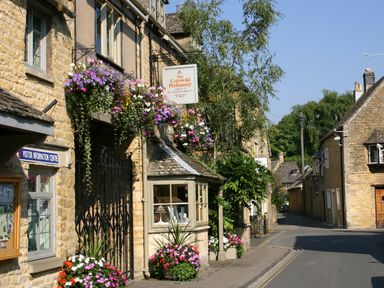 A street with stone buildings and flower arrangements at The Cotswold Perfumery in Bourton-on-the-Water