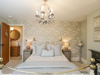 A bedroom with a metal bed frame bathed with pillows and lamps on bedside tables at Puffitts Cottage in Bourton-on-the-Water