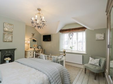 A bedroom with a bed a desk with a mirror a chair a window with blinds and a small armchair at Puffitts Cottage Bourton-on-the-Water