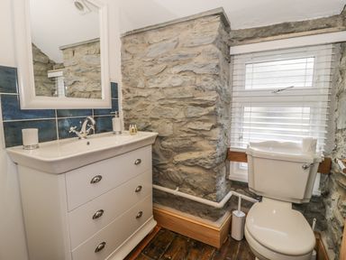 A bathroom with a white vanity and sink and a toilet beside a window with blinds at Garreg Ddu in Blaenau Ffestiniog