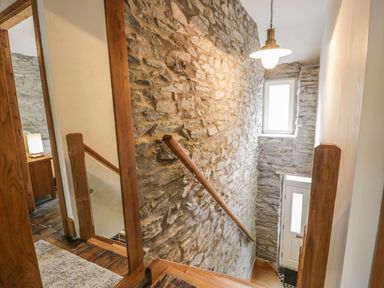 A staircase with wooden handrails and stone walls next to a white front door at Garreg Ddu in Blaenau Ffestiniog