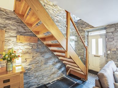 A stone wall entryway with wooden staircase wooden cabinet and a sofa at Garreg Ddu in Blaenau Ffestiniog