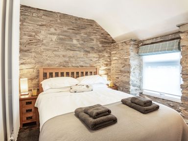 A bedroom with a wooden bed frame white bedding folded towels on the bed stone walls and a window with a blind at Garreg Ddu in Blaenau Ffestiniog