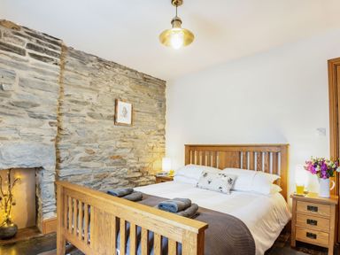 A bedroom with a wooden bed frame bedside tables and a stone wall at Garreg Ddu in Blaenau Ffestiniog