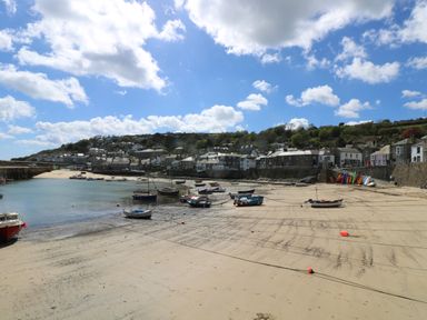 A beach with boats tied up on sand and a row of houses on a hill at Mermaid Cottage in Mousehole
