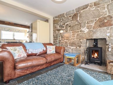 A living room with a leather sofa and a wood burning stove in a stone wall at Mermaid Cottage in Mousehole