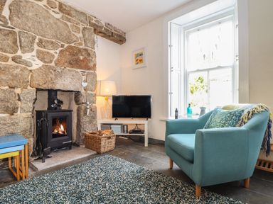 A living room with a stone fireplace a blue armchair and a television at Mermaid Cottage in Mousehole