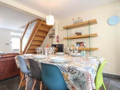 A dining room with a table set for six people and wooden stairs in the background at Mermaid Cottage in Mousehole