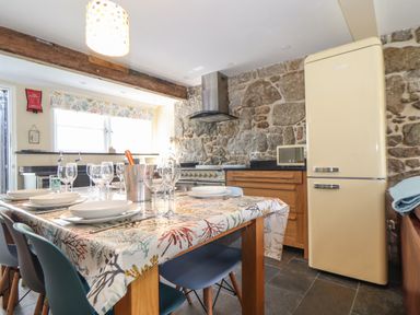 A kitchen with a dining table set with plates and glasses a refrigerator and stone walls at Mermaid Cottage in Mousehole