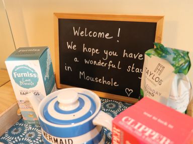A wooden tray with a blue and white teapot biscuits tea bags and a chalkboard with a welcome message at Mermaid Cottage in Mousehole