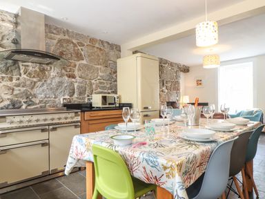 A kitchen with a stone wall a dining table set with plates glasses and chairs at Mermaid Cottage in Mousehole
