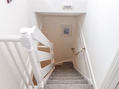 A carpeted staircase with white wooden railing and a rope handrail on the wall at Mermaid Cottage in Mousehole