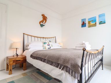 A bedroom with a bed with a gray blanket and pillows beside wooden nightstands with lamps at Mermaid Cottage in Mousehole