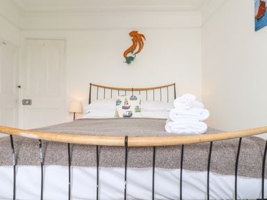A bedroom with a bed with patterned pillow and folded towels on the blanket at Mermaid Cottage in Mousehole