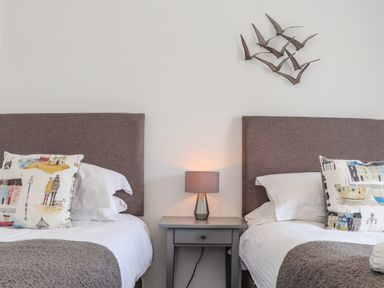 A bedroom with two single beds a gray nightstand and table lamp at Mermaid Cottage in Mousehole