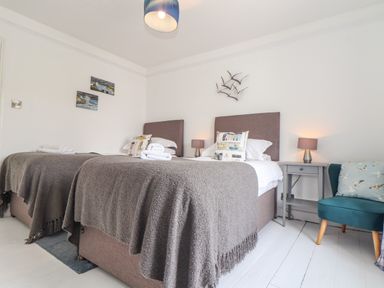 A bedroom with two single beds bedside tables with lamps a blue chair and bird wall decorations at Mermaid Cottage in Mousehole