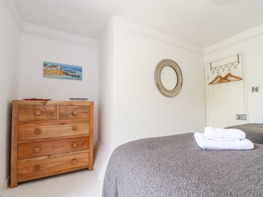 A bedroom with a wooden chest of drawers bed with folded towels a round mirror and a door with hangers at Mermaid Cottage in Mousehole