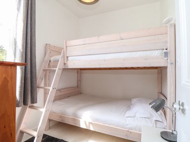 A bedroom with a wooden bunk bed white bedding a desk lamp a wooden chest of drawers and gray curtains at Mermaid Cottage in Mousehole