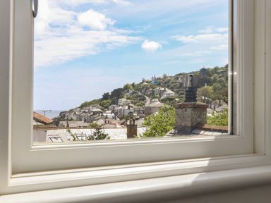 A window view showing rooftops and houses on a hillside under a blue sky at Mermaid Cottage in Mousehole
