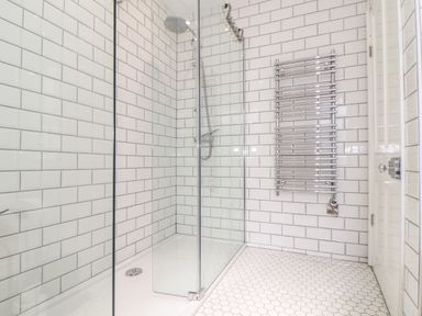 A walk in shower with glass doors white subway tiles and a chrome towel radiator at Mermaid Cottage in Mousehole