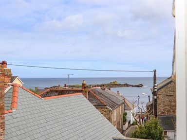 Rooftops of stone houses with chimneys and a view of the sea and rocky coast at Mermaid Cottage in Mousehole