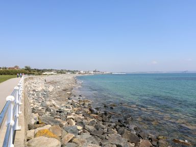 A rocky shoreline with a paved walkway and people walking by the sea at Mermaid Cottage in Mousehole