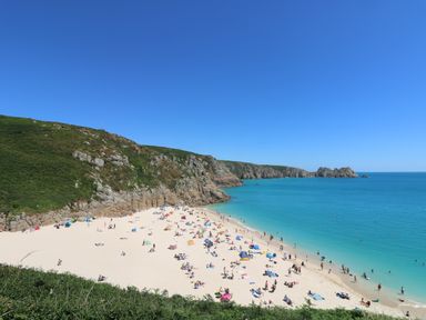 A sandy beach with people sunbathing and swimming surrounded by cliffs at Mermaid Cottage in Mousehole