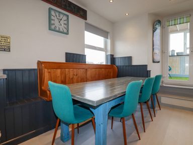 A dining area with a blue wooden table surrounded by turquoise chairs and a wooden bench at Sailor's Rest in Newquay