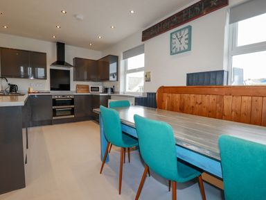 A kitchen with dark cabinets a double oven a table with teal chairs and wooden bench seating at Sailor's Rest in Newquay