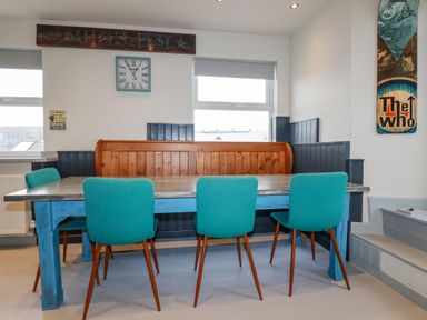 A dining area with a blue wooden table turquoise chairs and a wooden bench at Sailor's Rest in Newquay