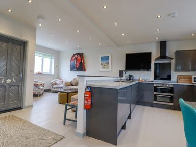 A kitchen with dark cabinets and a living room with printed armchairs and a beige sofa at Sailor's Rest in Newquay