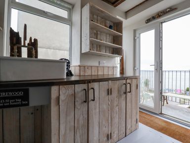 A kitchen area with wooden cabinets a white sink and a glass door leading to a balcony with ocean view at Sailor's Rest in Newquay