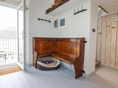 A corner wooden bench with a pet bed underneath near an open door and a wooden wall with hooks at Sailor's Rest in Newquay