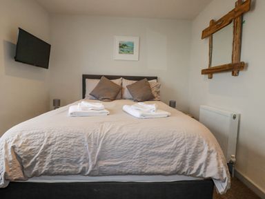 A bedroom with a bed with pillows and towels a mounted TV a framed picture and a wooden framed mirror at Sailor's Rest in Newquay