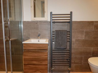 A bathroom with a wooden vanity sink cabinet a towel hanging on a heated towel rail and a glass shower enclosure at Sailor's Rest in Newquay