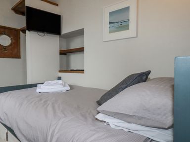 A small bedroom with a bed towels on bed wall-mounted TV and shelves a framed picture on the wall at Sailor's Rest in Newquay
