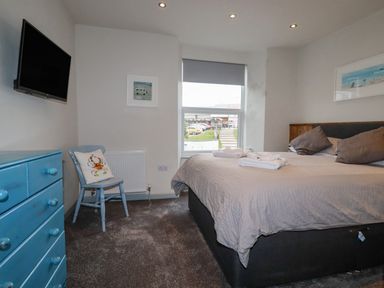 A bedroom with a bed a chair a blue dresser and a wall mounted TV at Sailor's Rest in Newquay
