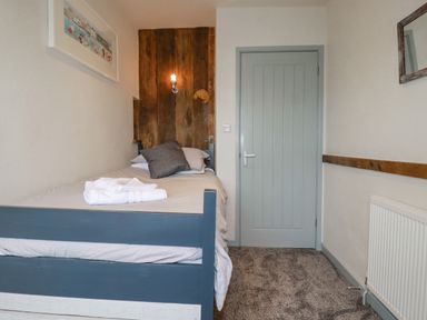 A bedroom with a single bed near a closed door and a wall light over a wooden panel at Sailor's Rest in Newquay