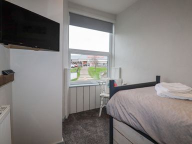 A small bedroom with a single bed a chair under a window and a wall-mounted television at Sailor's Rest in Newquay