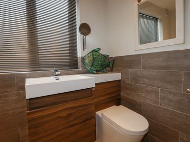A bathroom with a toilet and a sink with wooden cabinets and a green fish decoration at Sailor's Rest in Newquay