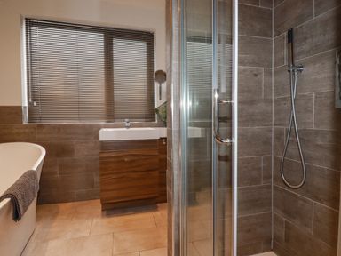 A bathroom with a shower enclosure a bathtub a sink with a wooden cabinet and a window with blinds at Sailor's Rest in Newquay