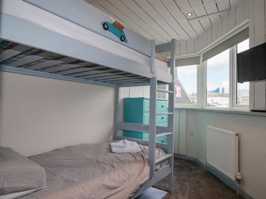 A bedroom with a blue bunk bed a dresser window and a wall-mounted tv at Sailor's Rest in Newquay