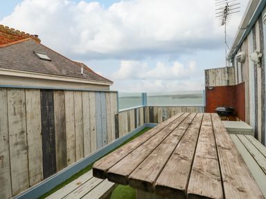 An outdoor seating area with a wooden picnic table bench a barbecue and a view of a cloudy sky at Sailor's Rest in Newquay