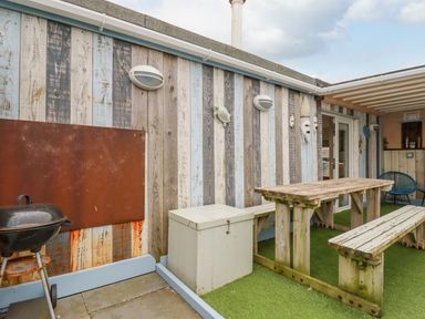 An outdoor seating area with a wooden picnic table and benches a barbecue and a small white storage box at Sailor's Rest in Newquay