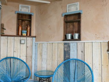 A room with two blue round chairs and a glass top table with wooden shelves on the wall with decorative items at Sailor's Rest in Newquay