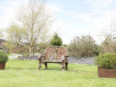 A garden with a rustic wooden bench between two potted plants and trees in the background at 16 Badgers Retreat in Richmond